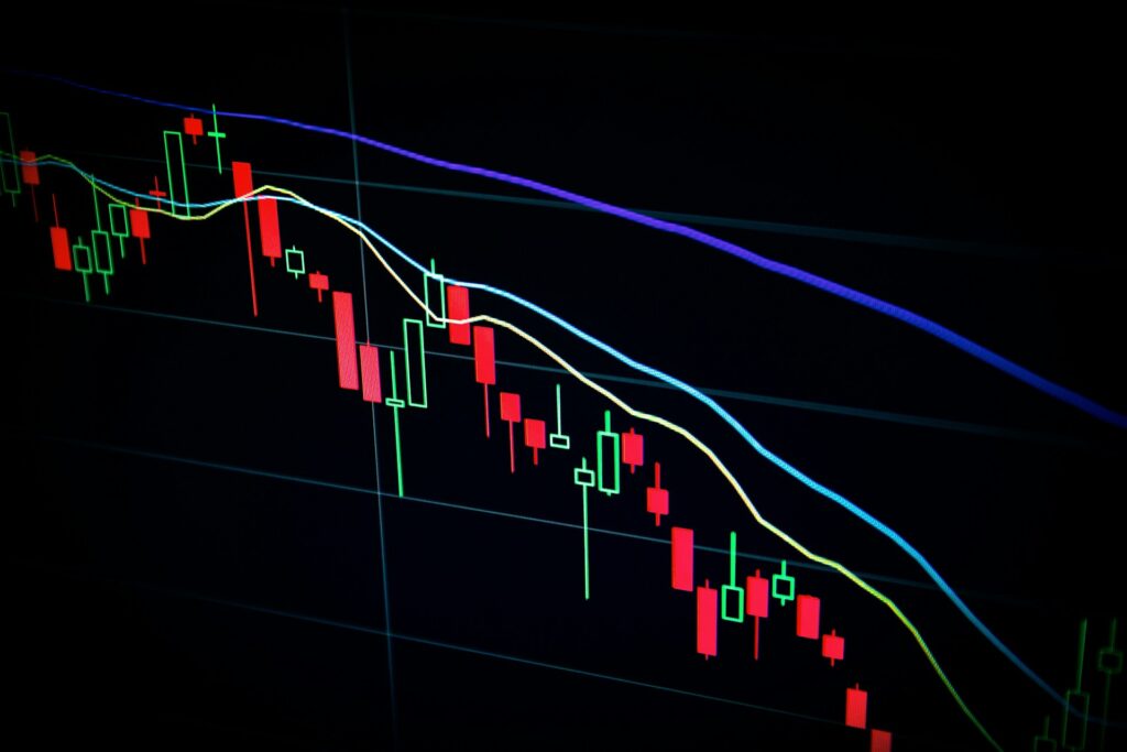 Red and green candlestick trading chart with moving average lines on a dark screen showing a downward trend
