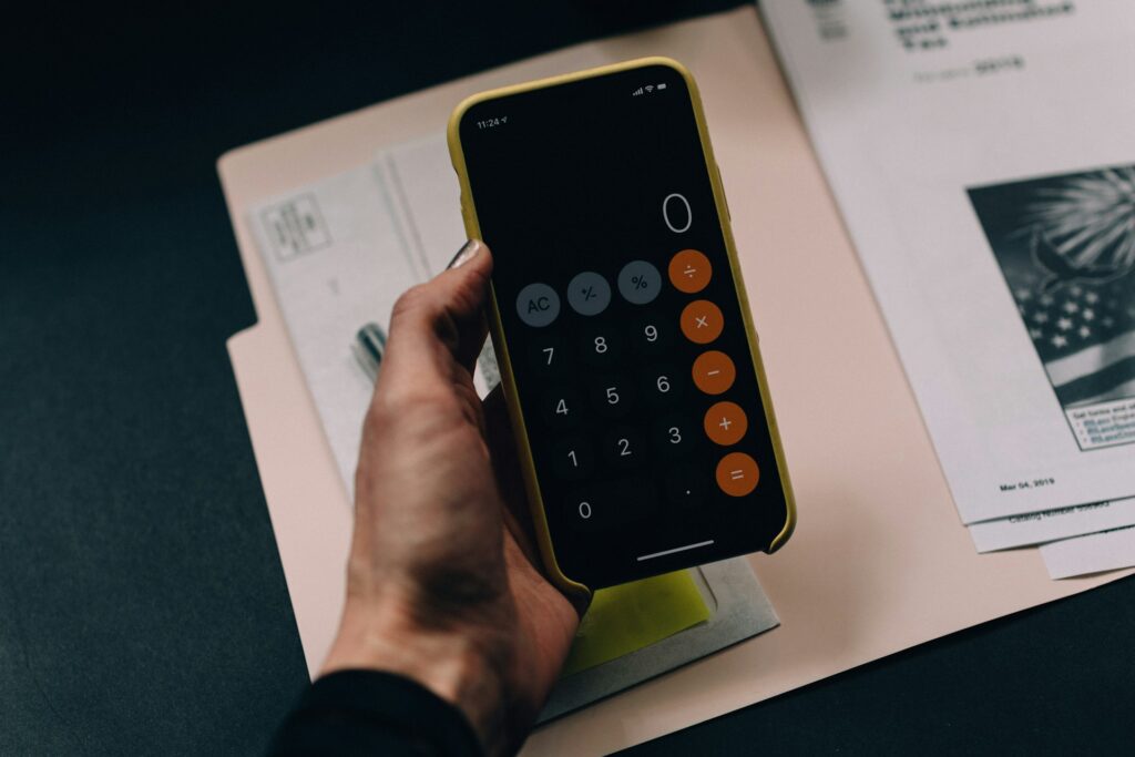 An aesthetic shot of someone holding their iphone with the calculator open, with files on the desk behind