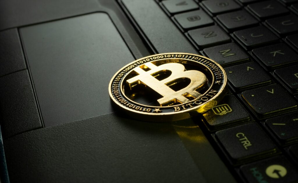 Gold bitcoin coin resting on a dark laptop keyboard with binary code engraved around the edge