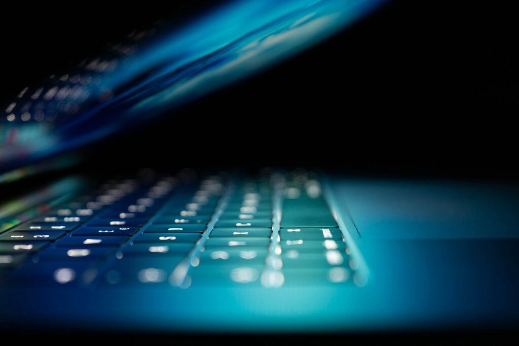 A close-up of a closed laptop in a dark room with blue screen light glowing