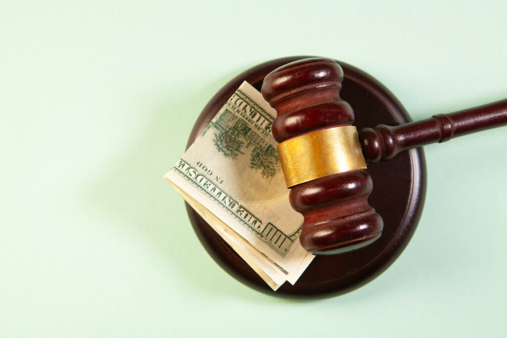 Wooden judge's gavel resting on us dollar bills on a sound block against a light green background