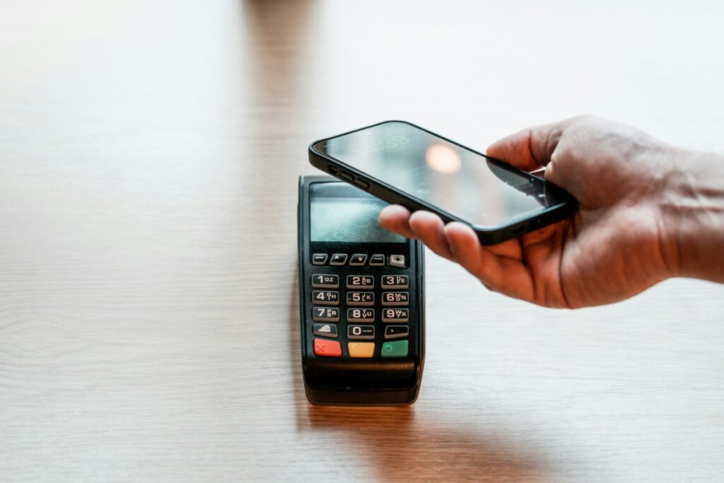 A hand holds a smartphone over a card reader to make a digital payment