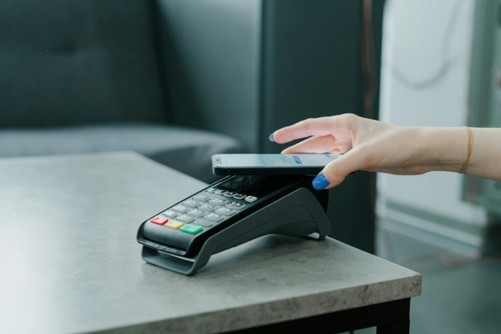 Hand holding a smartphone over a contactless card payment terminal on a grey countertop
