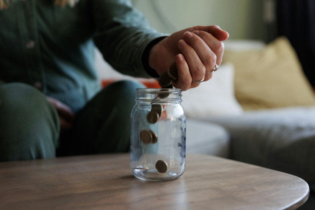 A close-up of a hand in a living room pouring coins into a glass savings pot