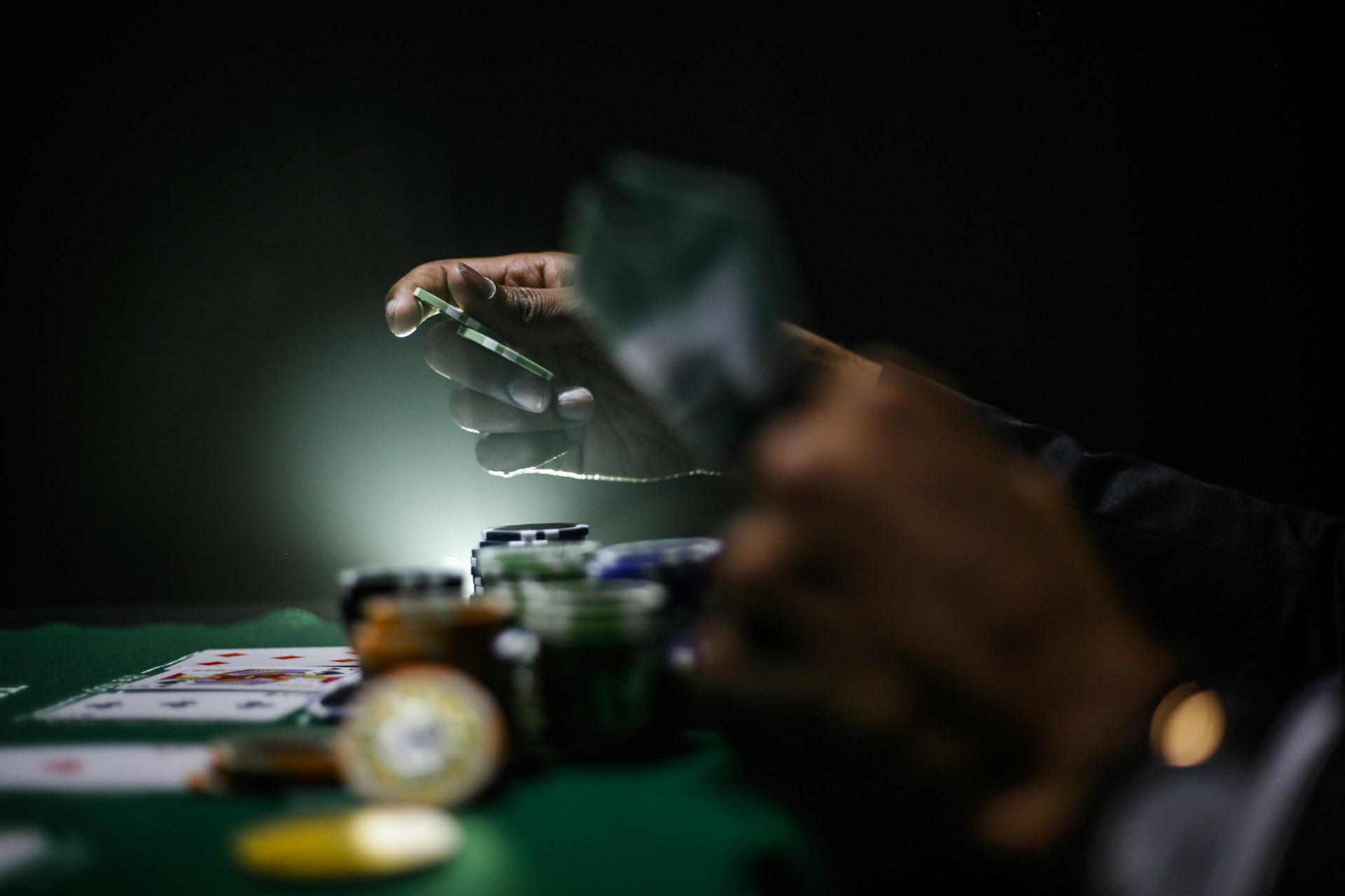 Hand placing a poker chip on a green felt table with stacked chips and playing cards in low light