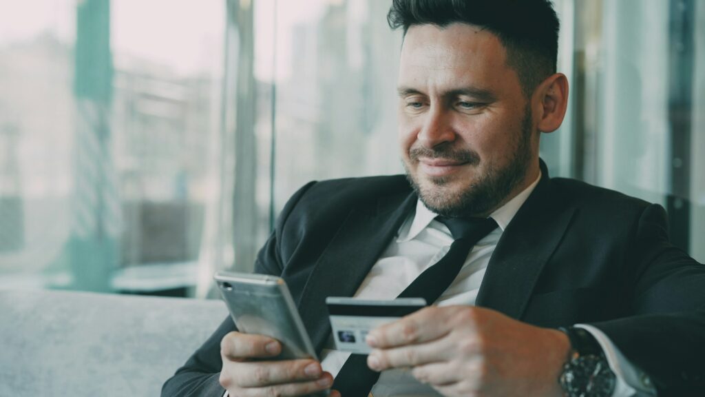 Businessman using his phone and bank card by a city window, representing a fintech founder navigating emi safeguarding