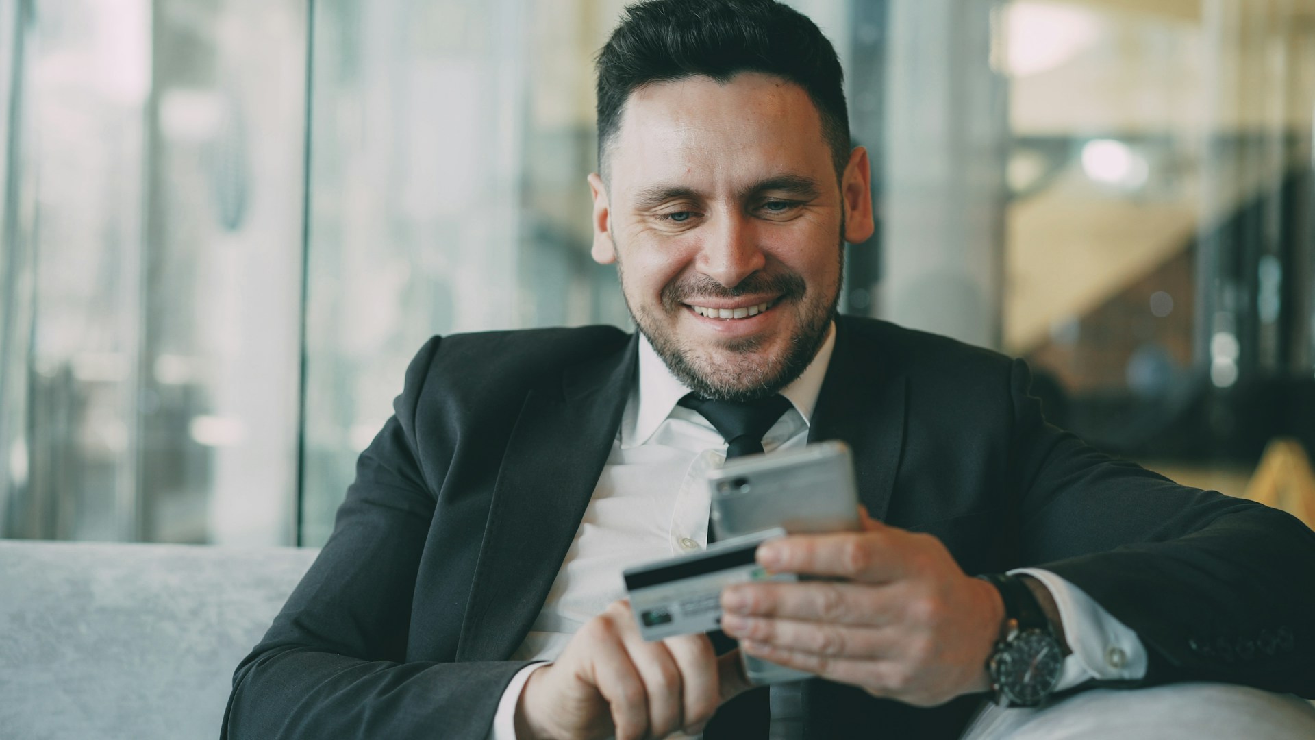 A business manager smiles while using a smartphone to manage a successful account that hasn't declined