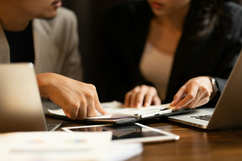 Two colleagues reviewing business documents together at a desk with laptops