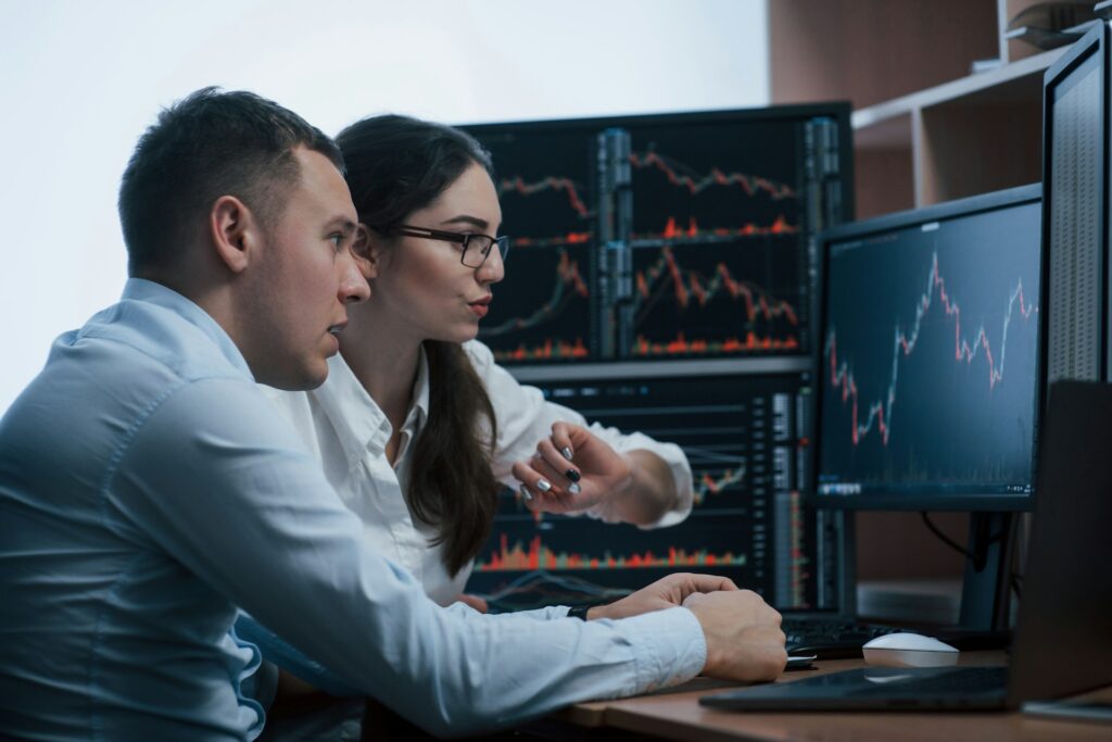 Two colleagues discussing market charts across multiple trading monitors
