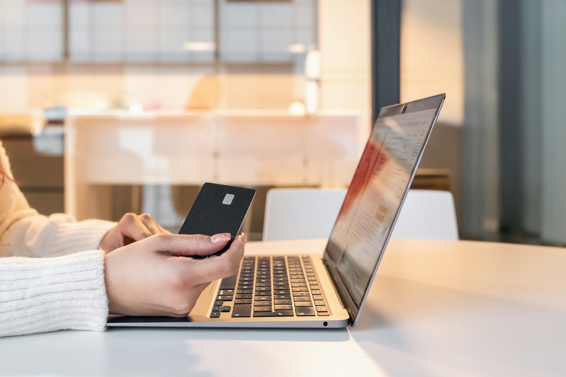 Person holding a bank card while using online banking on a laptop